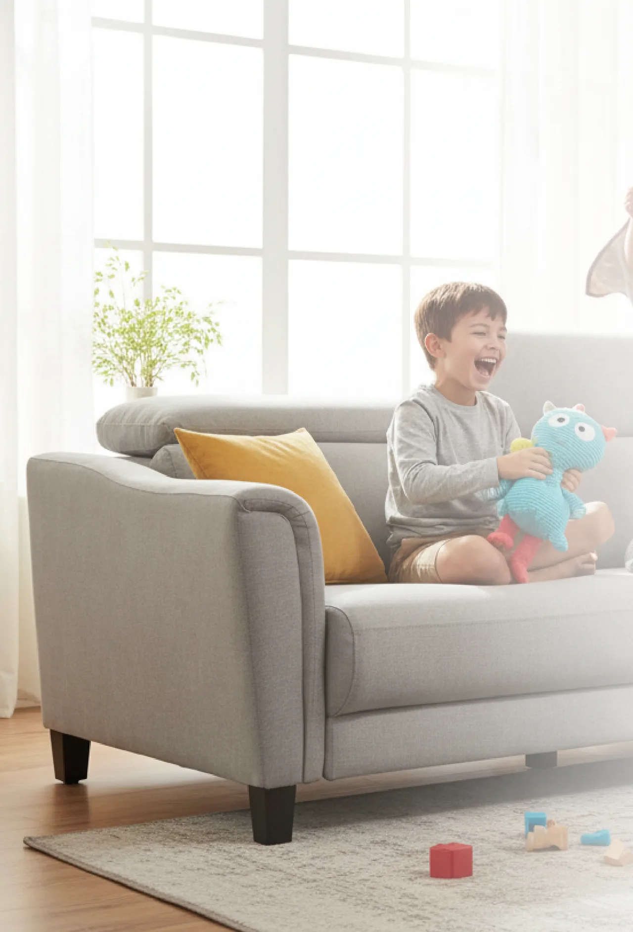 A child playing on a light grey alecca sofa in a bright living room